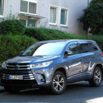 A grey toyota parallel parked up against a bush